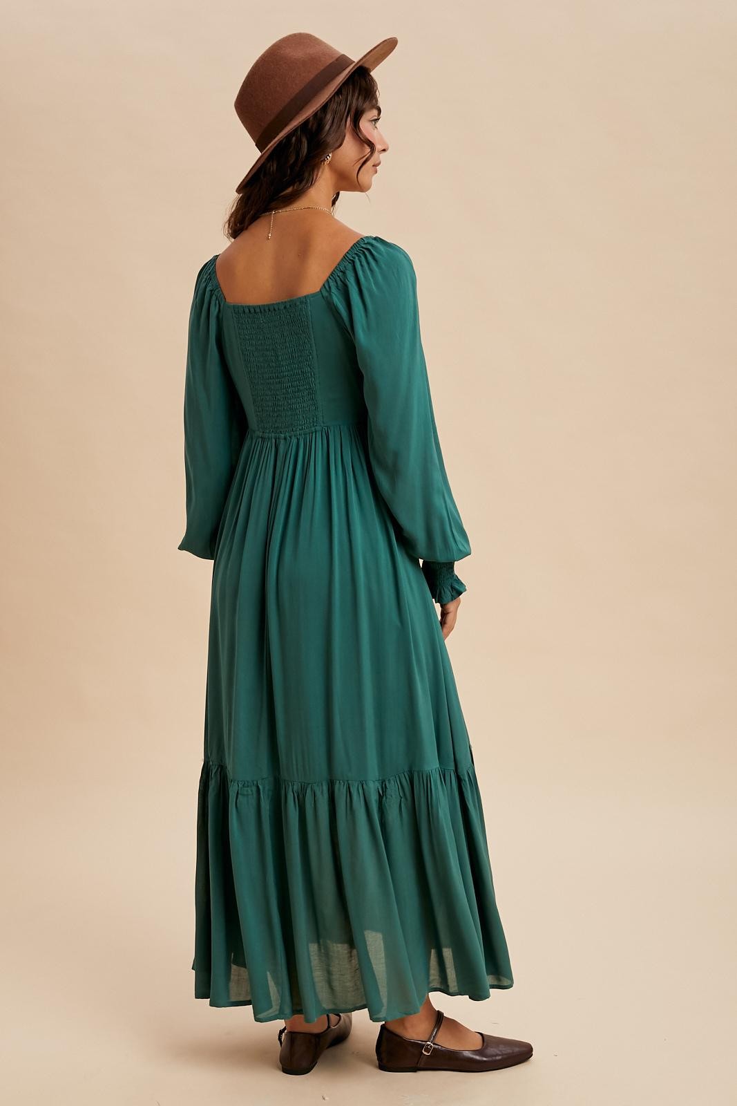 woman wearing a green long sleeve maxi dress with smocked back and ruffled hem, styled with a brown hat and shoes