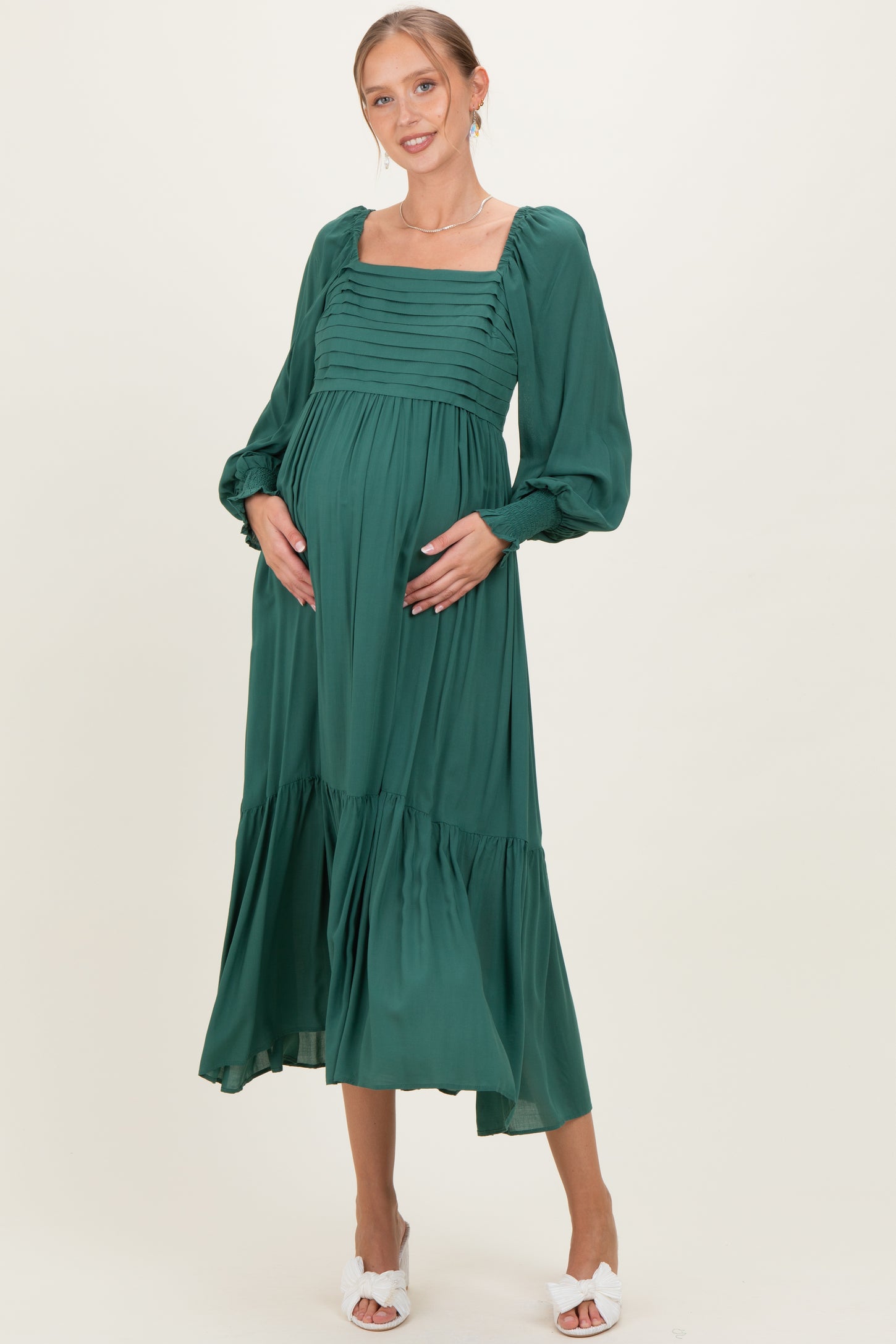woman wearing a green maternity dress with a square neckline and balloon sleeves, holding her baby bump