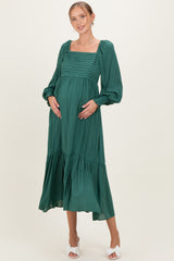 woman wearing a green maternity dress with a square neckline and balloon sleeves, holding her baby bump