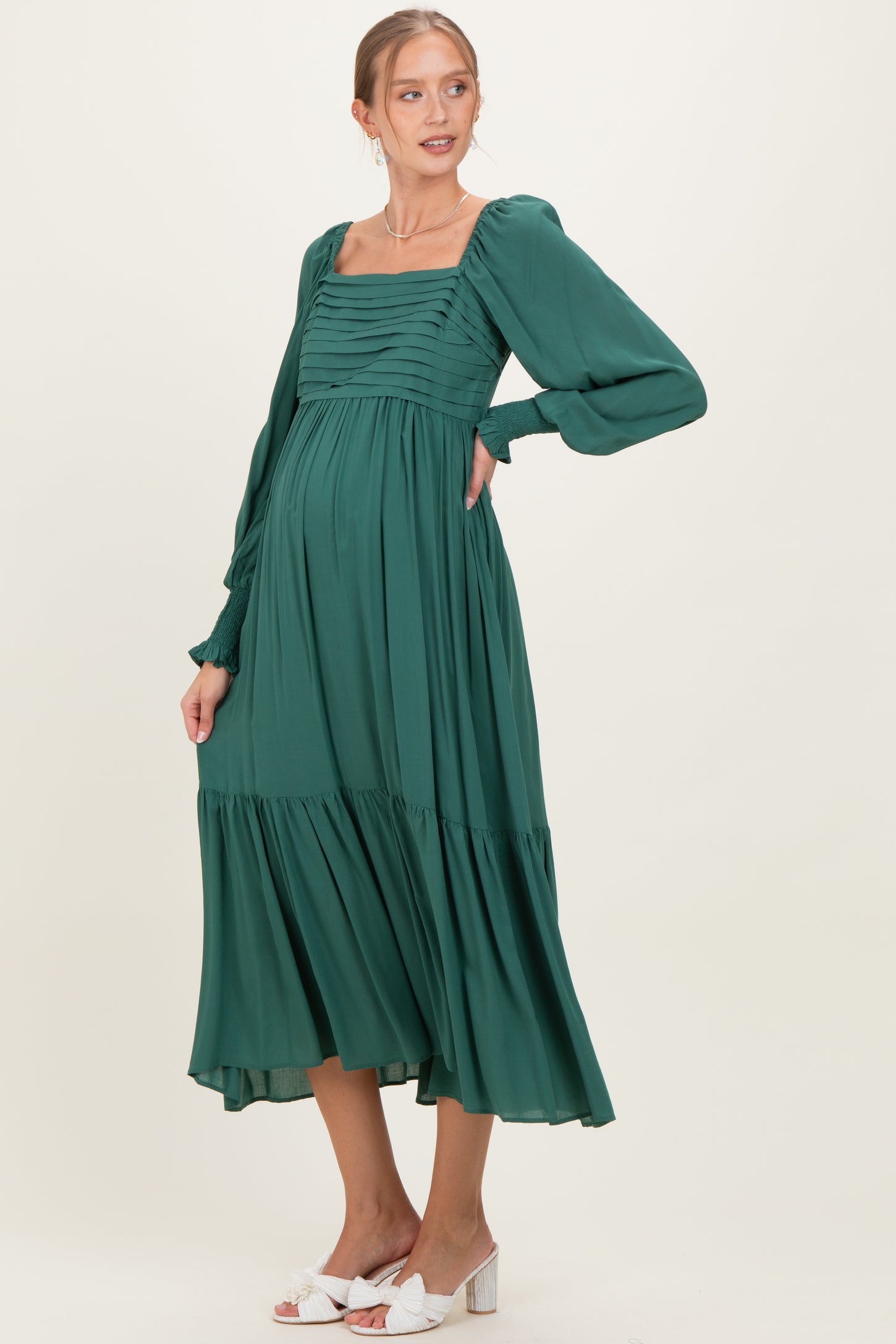 woman wearing a green maternity dress with puff sleeves, square neckline, and flowing skirt, highlighting her baby bump
