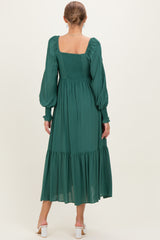 woman wearing a dark green maternity maxi dress with puff sleeves and a smocked bodice, showing a flowing tiered skirt