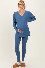 woman wearing a blue long sleeve maternity top and matching leggings, smiling and holding her baby bump