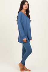 woman wearing a blue long sleeve pullover and matching leggings, standing barefoot against a light background