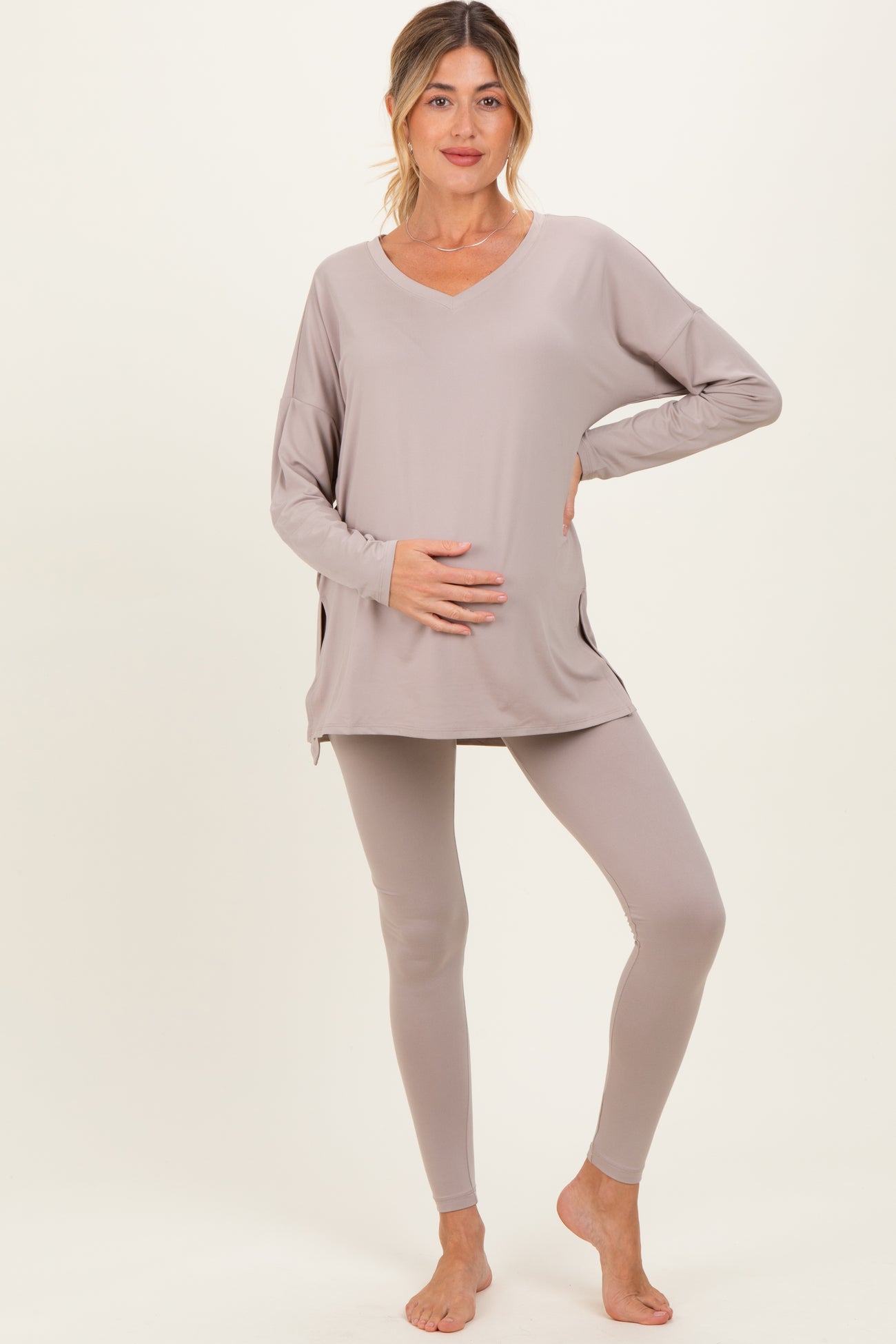 woman wearing a taupe maternity long sleeve top and matching leggings, holding her baby bump