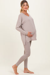 woman wearing a taupe maternity top and matching leggings, gently holding her baby bump