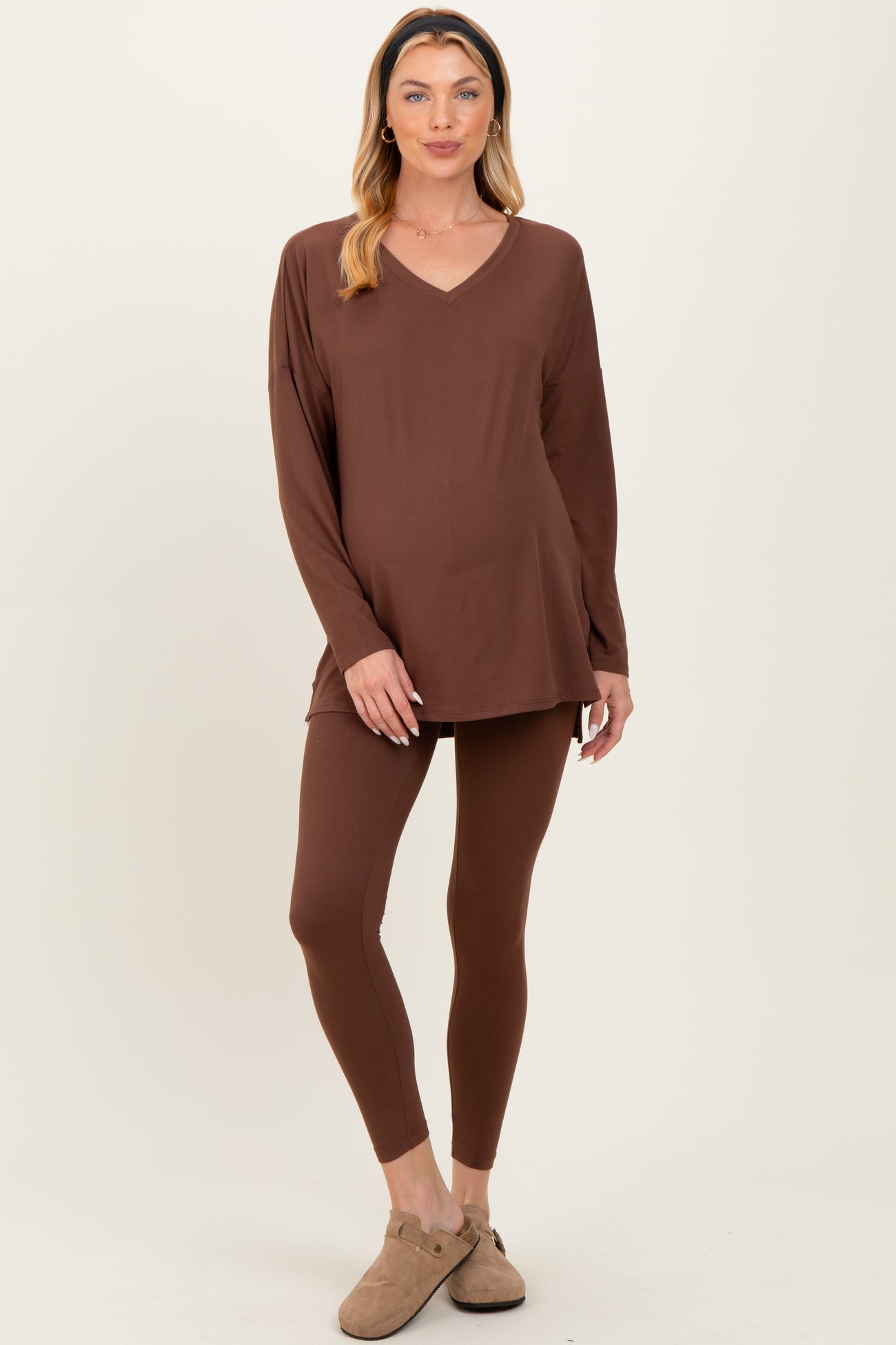 woman wearing a brown maternity loungewear set with a v-neck long sleeve top and fitted leggings, showing her baby bump