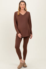 woman wearing a brown maternity loungewear set with a v-neck long sleeve top and fitted leggings, showing her baby bump