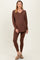 woman wearing a brown maternity loungewear set with a v-neck long sleeve top and fitted leggings, showing her baby bump