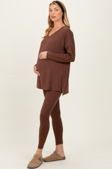woman wearing a brown maternity tunic and matching leggings, gently holding her baby bump