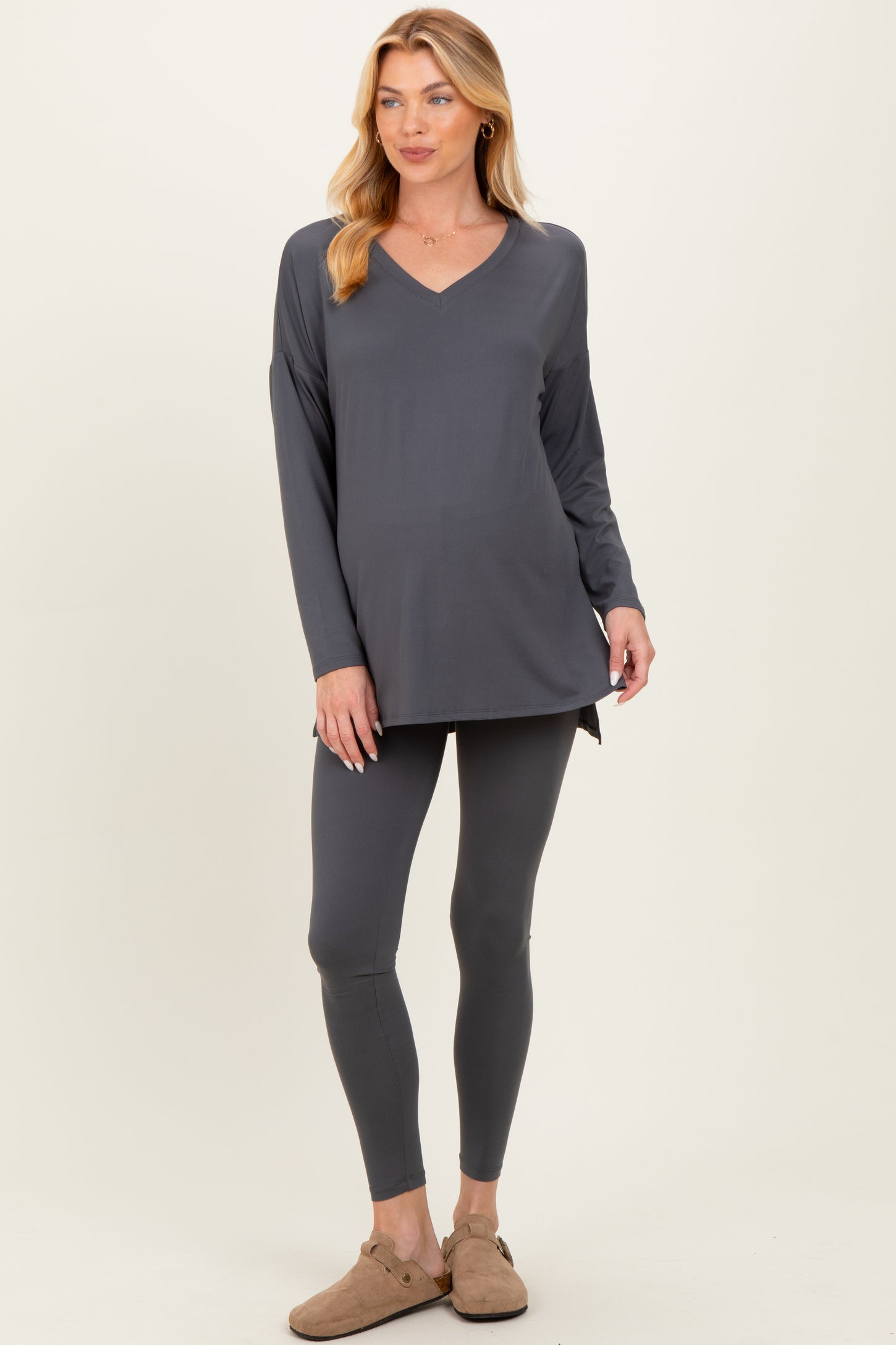 woman wearing a dark gray maternity top with a v-neck and long sleeves, paired with matching leggings and casual footwear