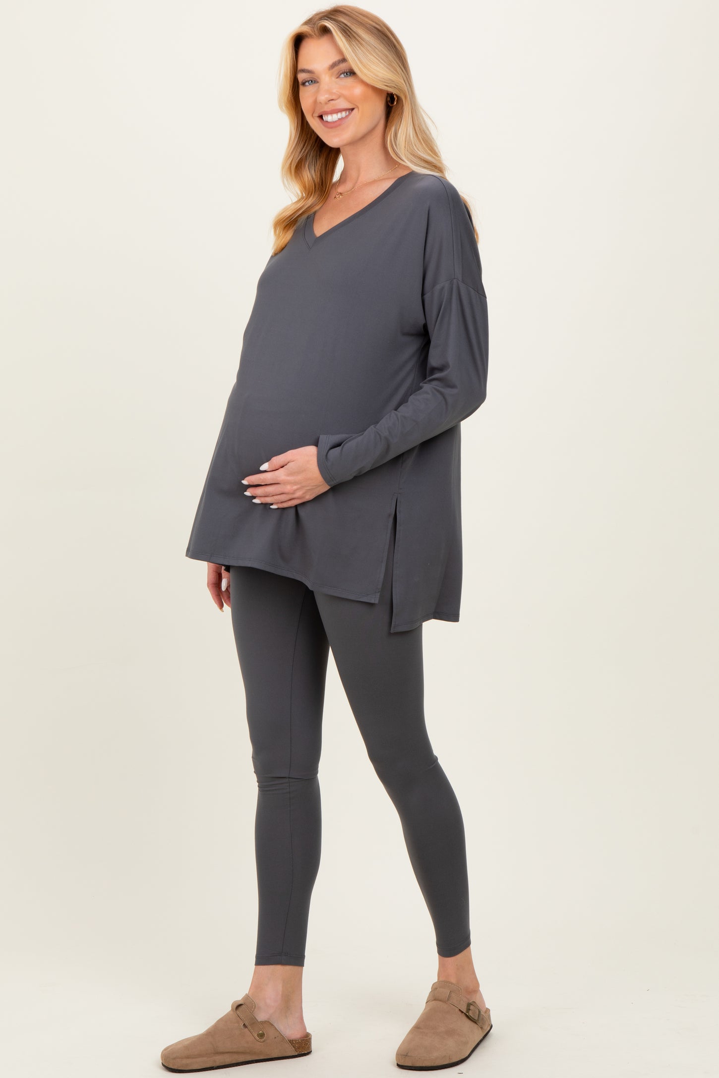 woman wearing a dark gray maternity top with side slits and matching leggings, showcasing her baby bump