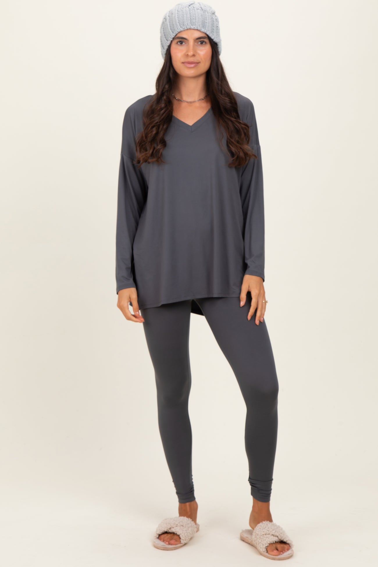 woman wearing a dark gray long sleeve top with a v-neck and matching leggings, styled with a knit beanie and fuzzy slippers