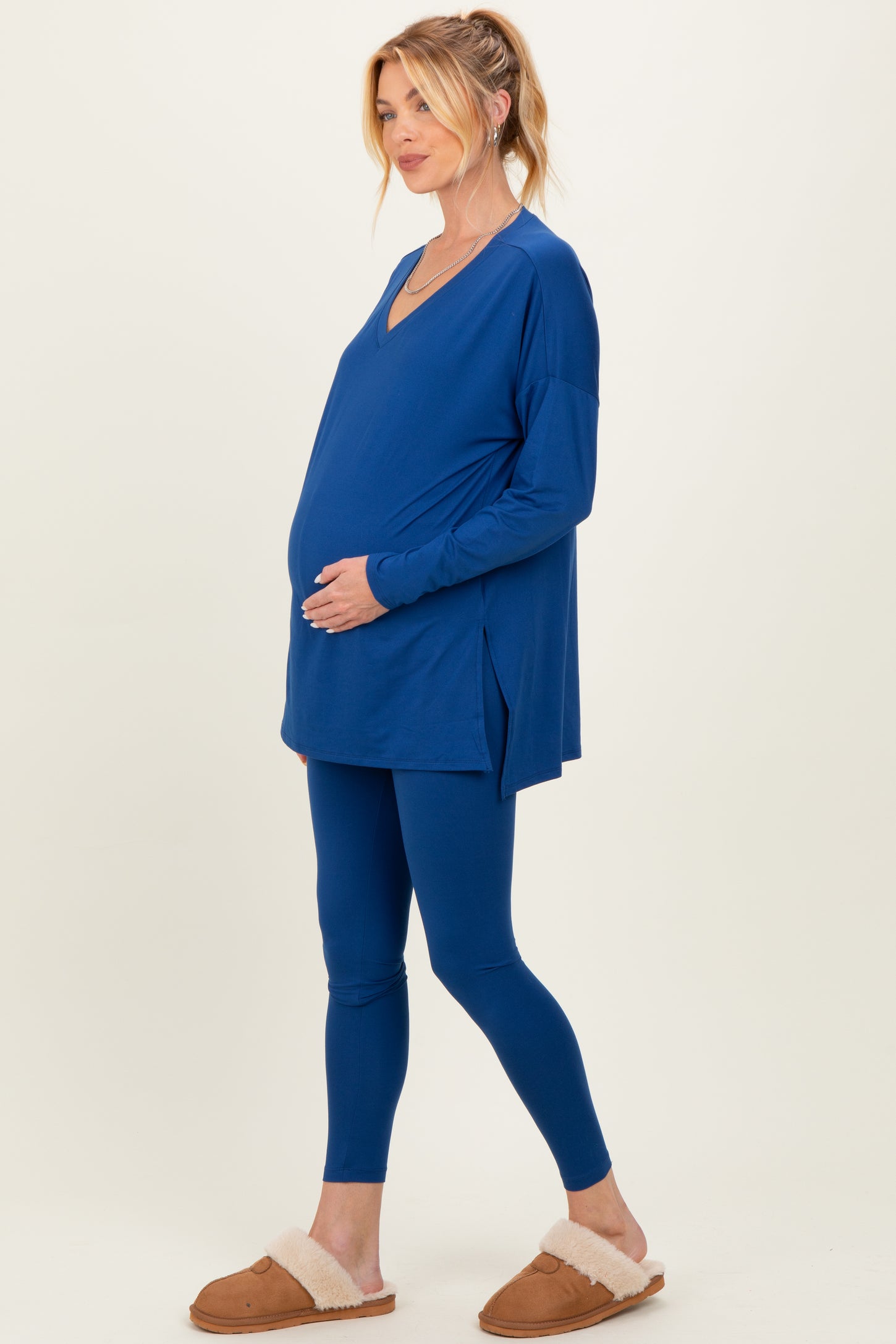 woman wearing a bright blue maternity top and leggings, showcasing her baby bump while standing in a relaxed pose