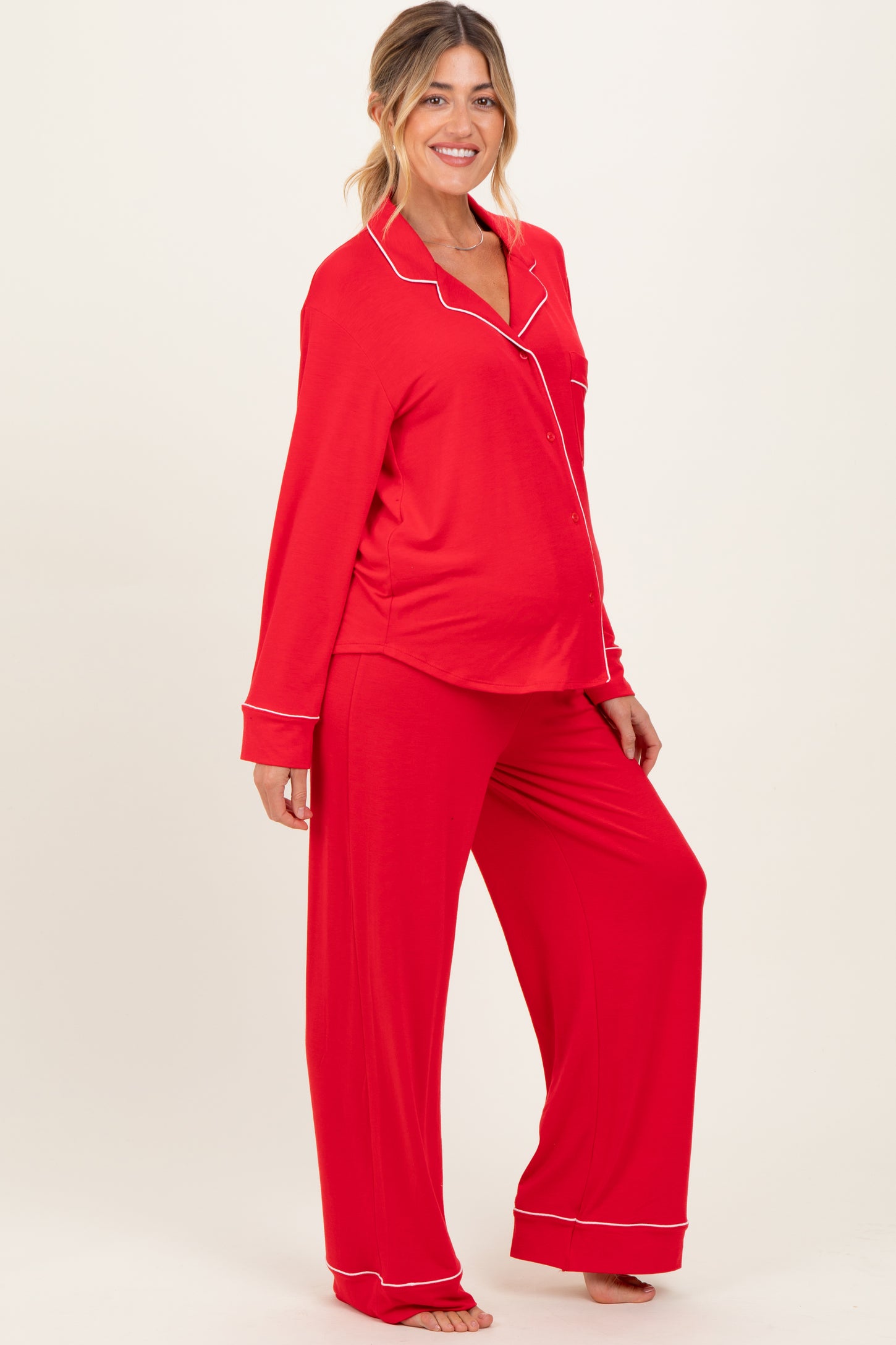 woman wearing a red maternity pajama set with white piping and a visible baby bump