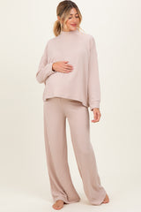 woman wearing a light pink ribbed long sleeve maternity top and matching wide-leg pants, gently cradling her baby bump