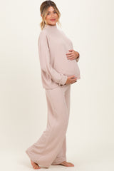 woman wearing a ribbed pink maternity loungewear set with a mock neck and wide-leg pants, holding her baby bump