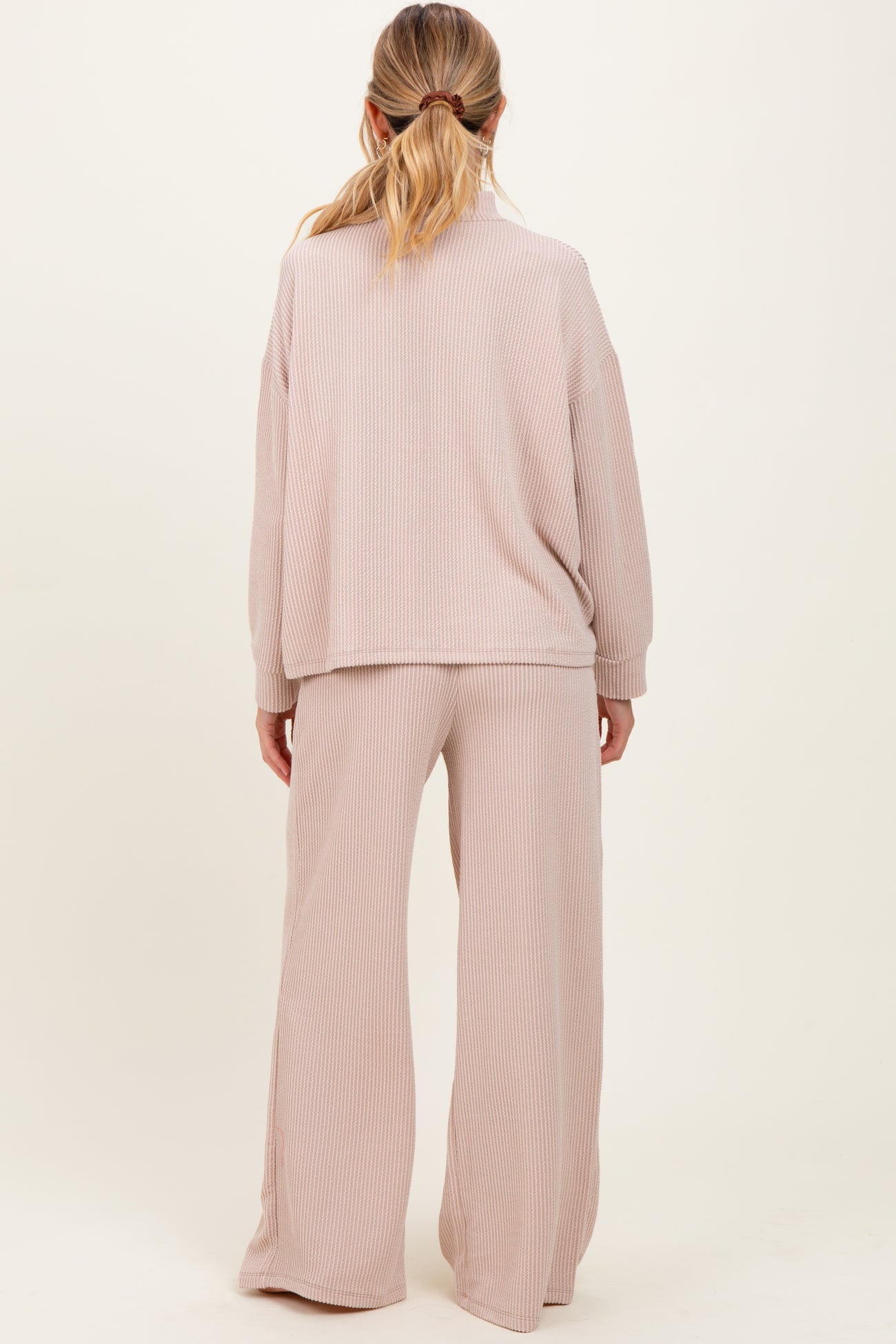 woman wearing a light pink ribbed maternity loungewear set, featuring a relaxed top and wide-leg pants from the back
