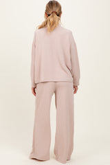 woman wearing a light pink ribbed maternity loungewear set, featuring a relaxed top and wide-leg pants from the back