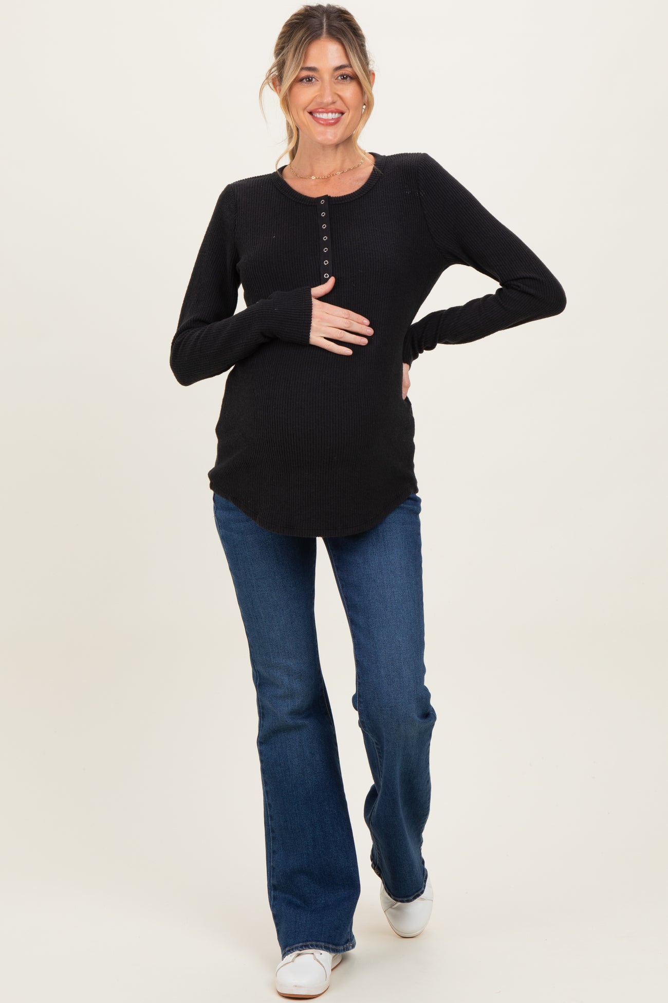 woman wearing a black maternity long sleeve top with buttons and blue flared jeans, showing her baby bump