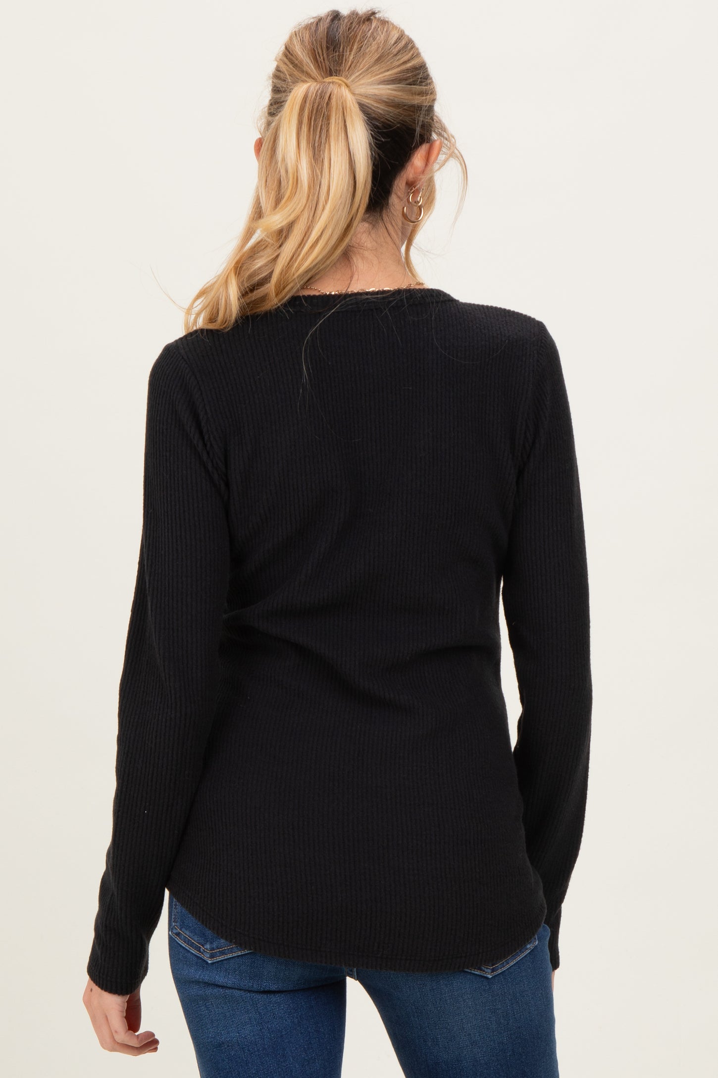 woman wearing a black long sleeve maternity top, viewed from the back, paired with blue jeans