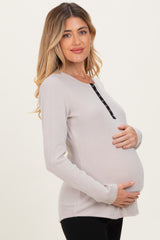 woman wearing a light gray ribbed maternity sweater with button details, holding her baby bump