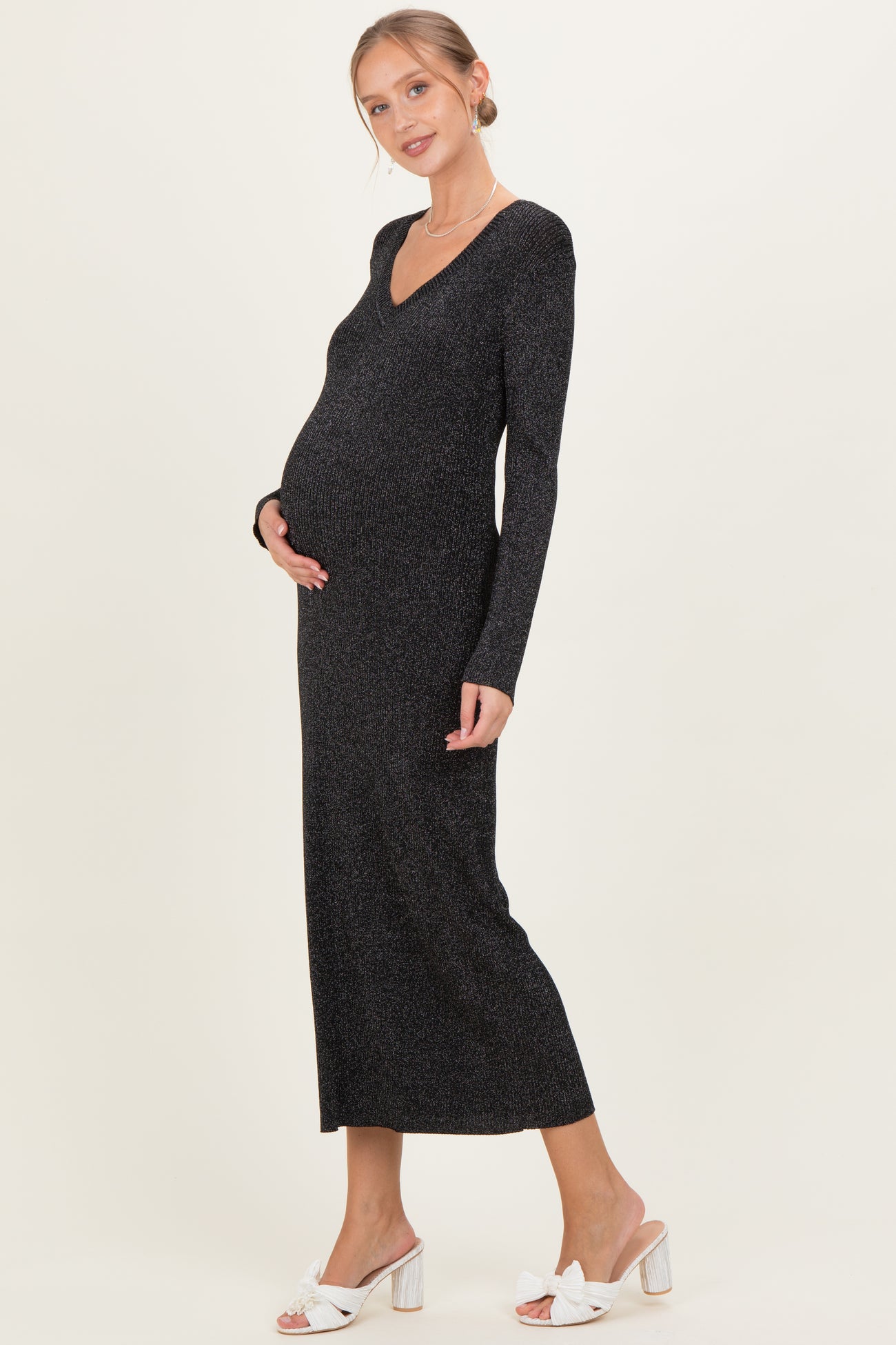 woman wearing a black sparkly long sleeve maternity dress and holding her baby bump