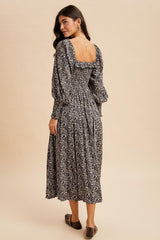 woman wearing a black floral midi dress with puff sleeves and a smocked back, posed from the back