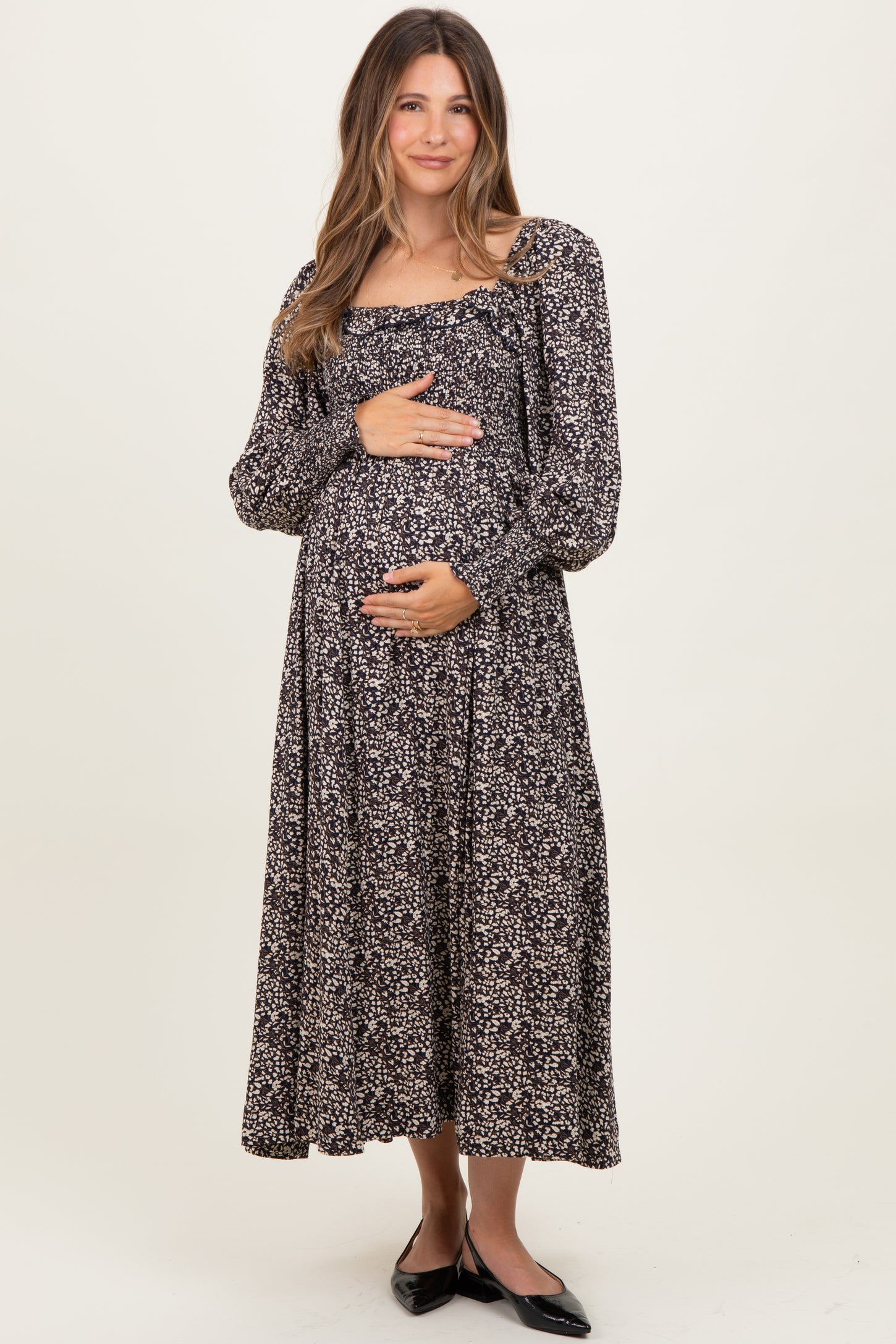 woman wearing a black floral maternity maxi dress and holding her baby bump