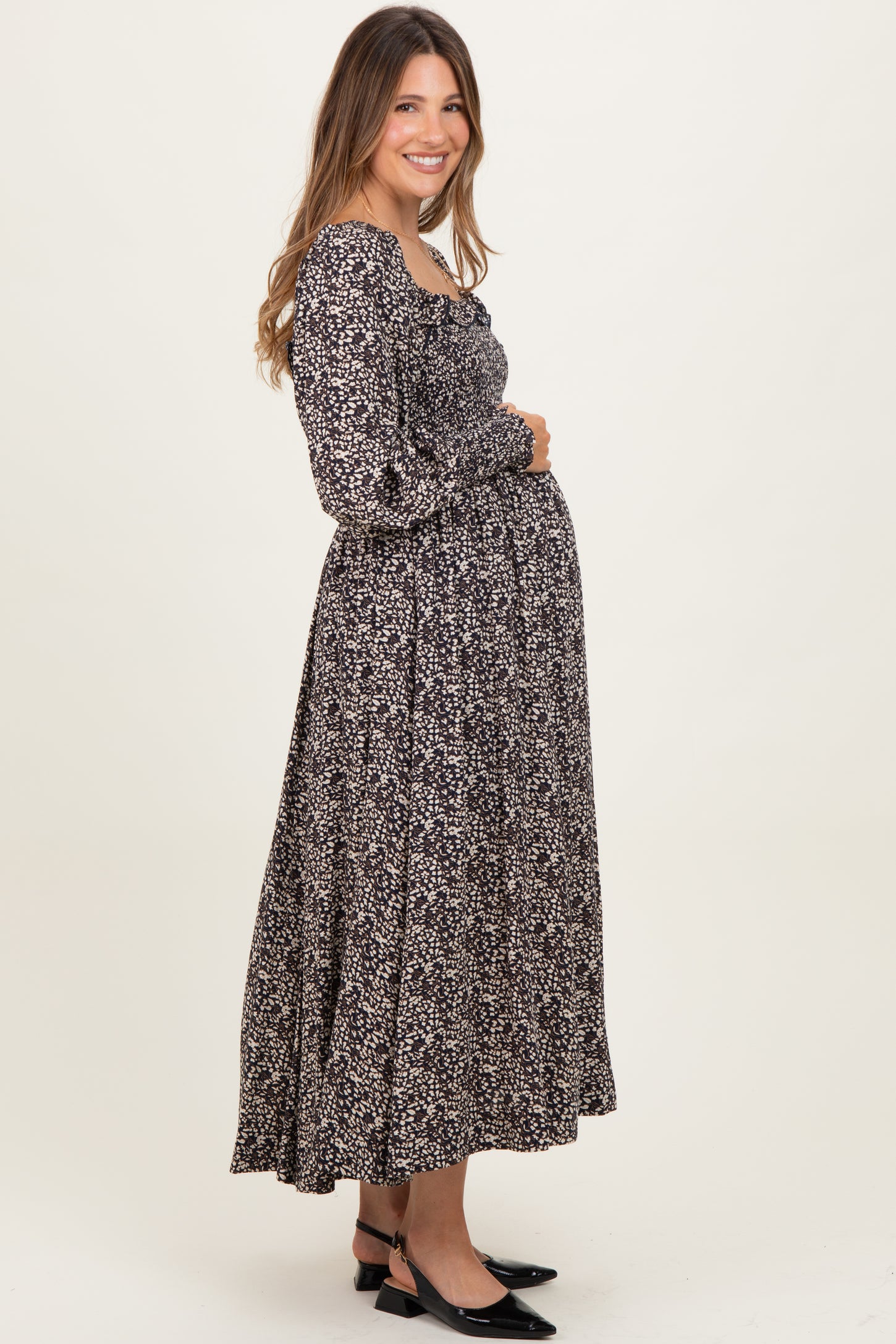 woman wearing a black floral maternity maxi dress and gently holding her baby bump