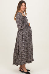woman wearing a black floral maternity maxi dress and gently holding her baby bump