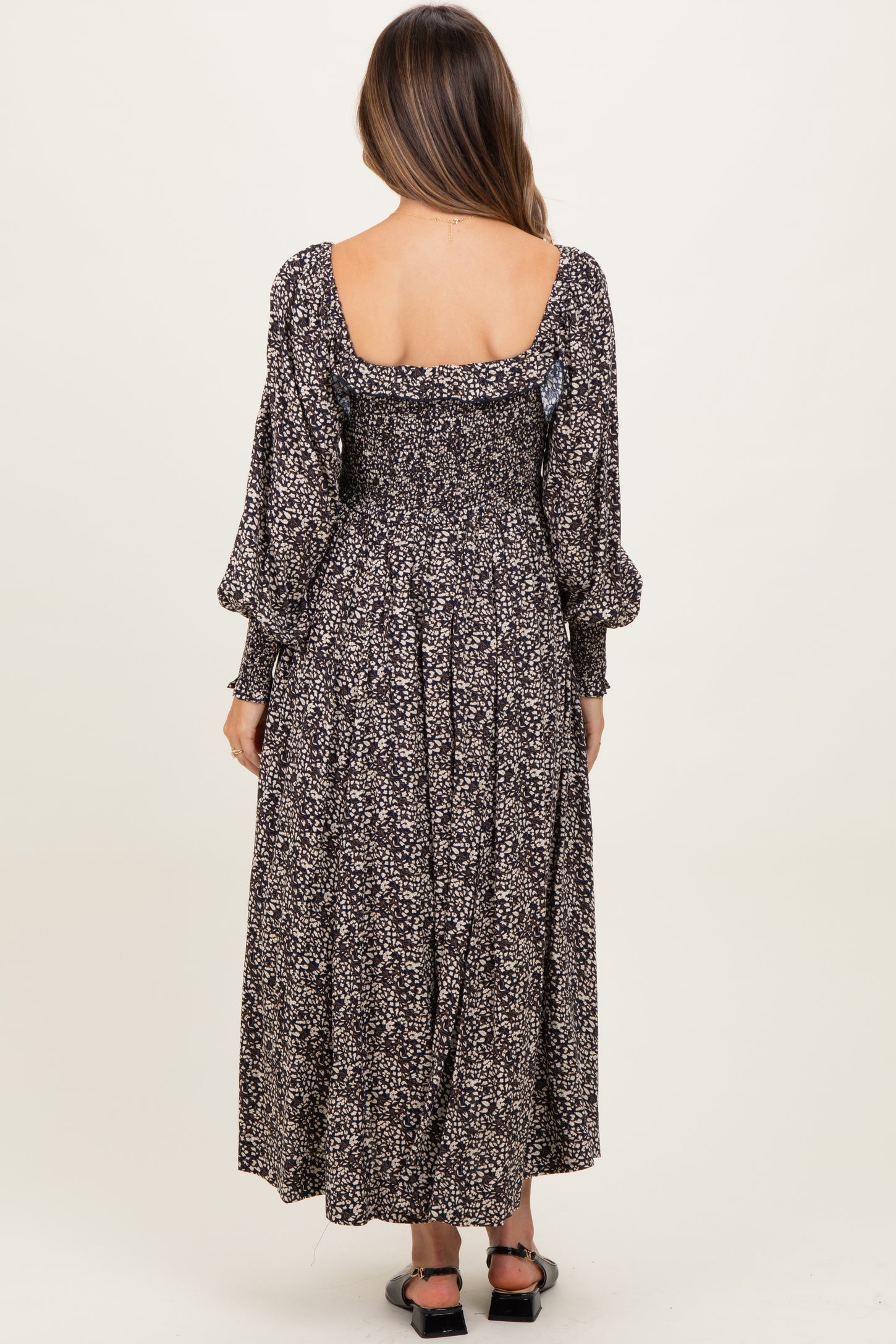 woman wearing a black floral maternity dress with puffed sleeves and a smocked back, showing her baby bump.