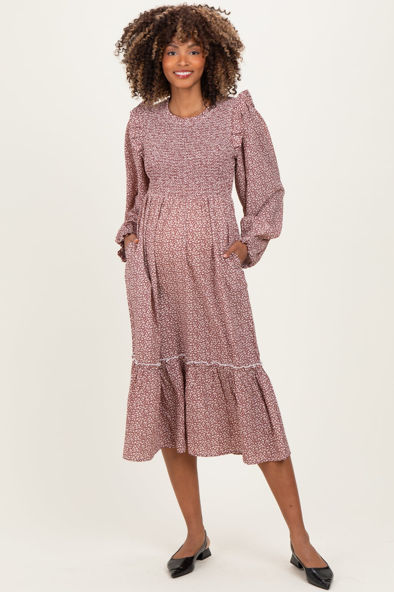 woman wearing a maroon floral print maternity dress with long sleeves and pockets, displaying her baby bump