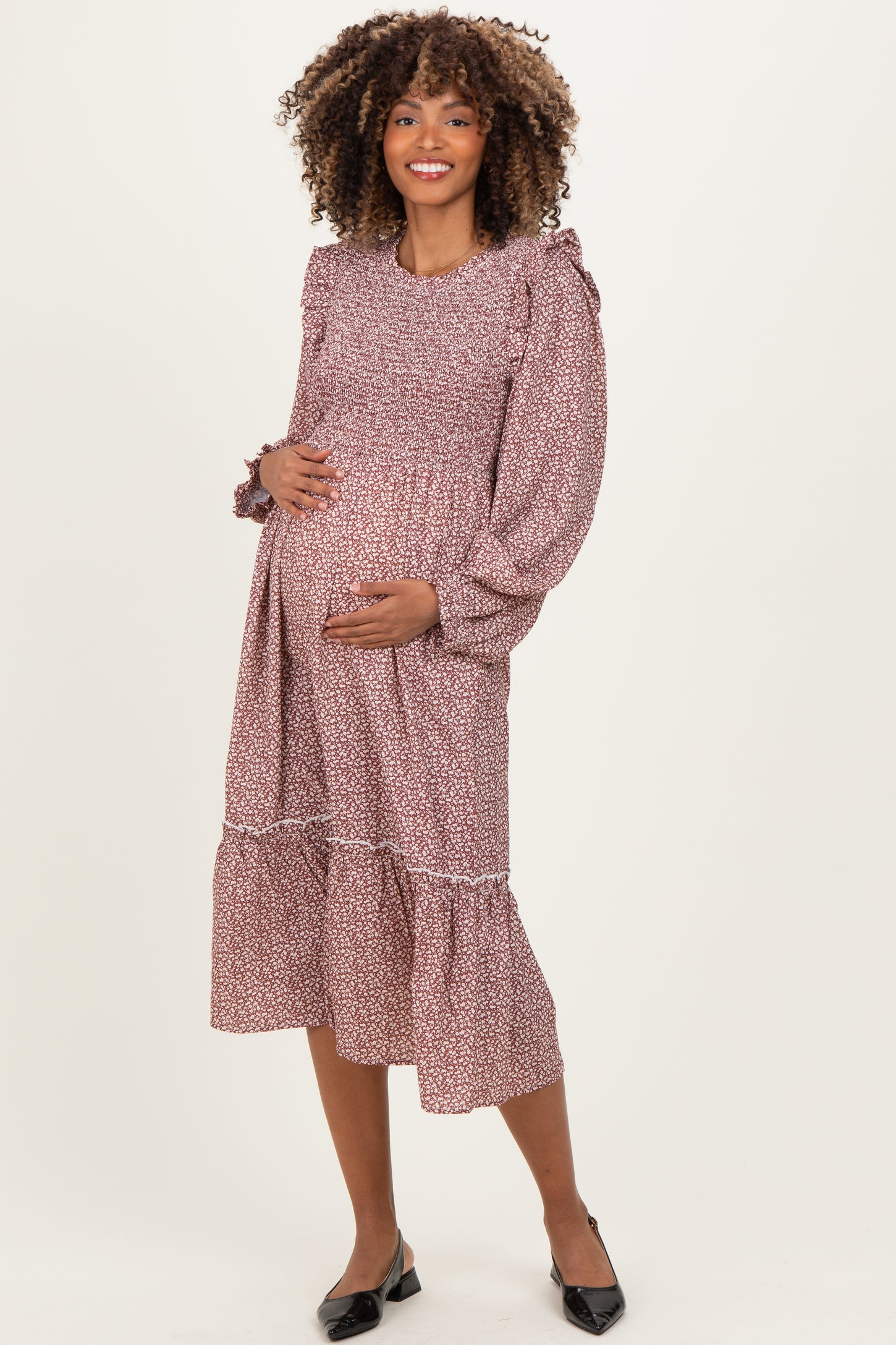 woman wearing a burgundy floral print maternity dress with long puff sleeves and a tiered hem, holding her baby bump