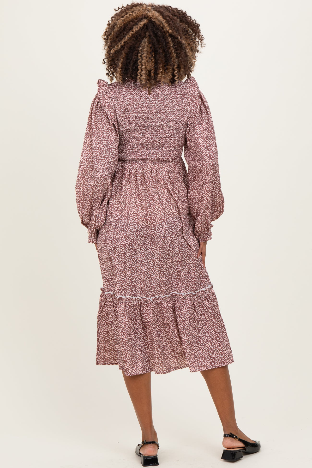 woman wearing a floral print maternity dress with puffed sleeves and a tiered skirt, showing a baby bump from the back