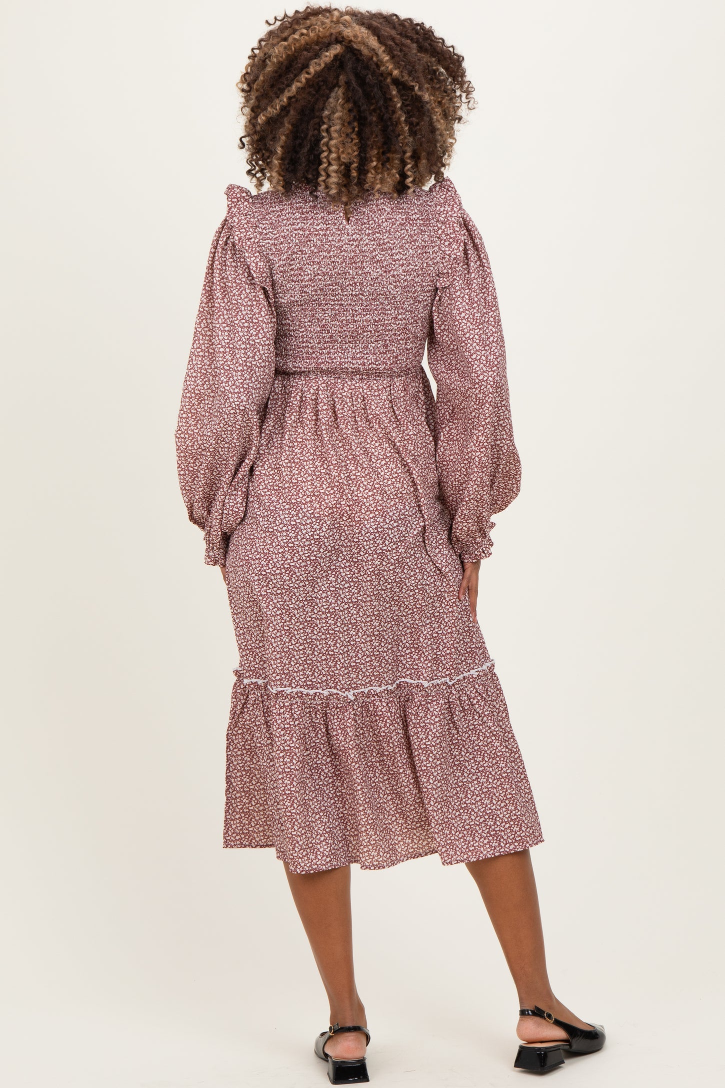 woman wearing a floral print maternity dress with puffed sleeves and a tiered skirt, showing a baby bump from the back