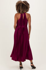 woman wearing a plum pleated maternity dress, showcasing a halter neck and flowy skirt from the back
