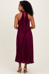woman wearing a sleeveless pleated burgundy dress with a halter neck and back tie detail, viewed from the back
