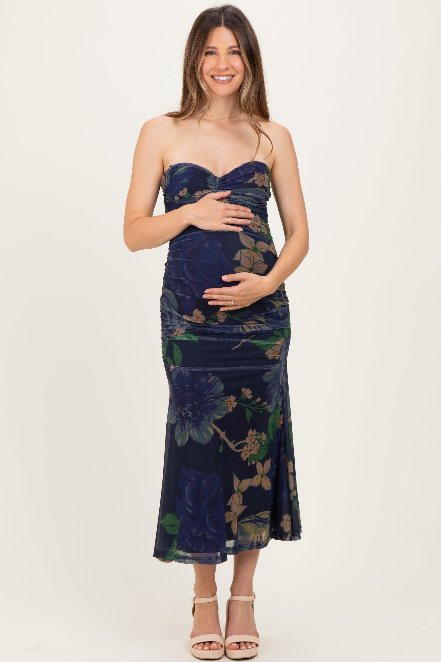 woman wearing a floral print navy maternity dress with a sweetheart neckline and ruched details, holding her baby bump