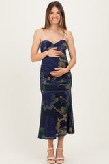 woman wearing a floral print navy maternity dress with a sweetheart neckline and ruched details, holding her baby bump