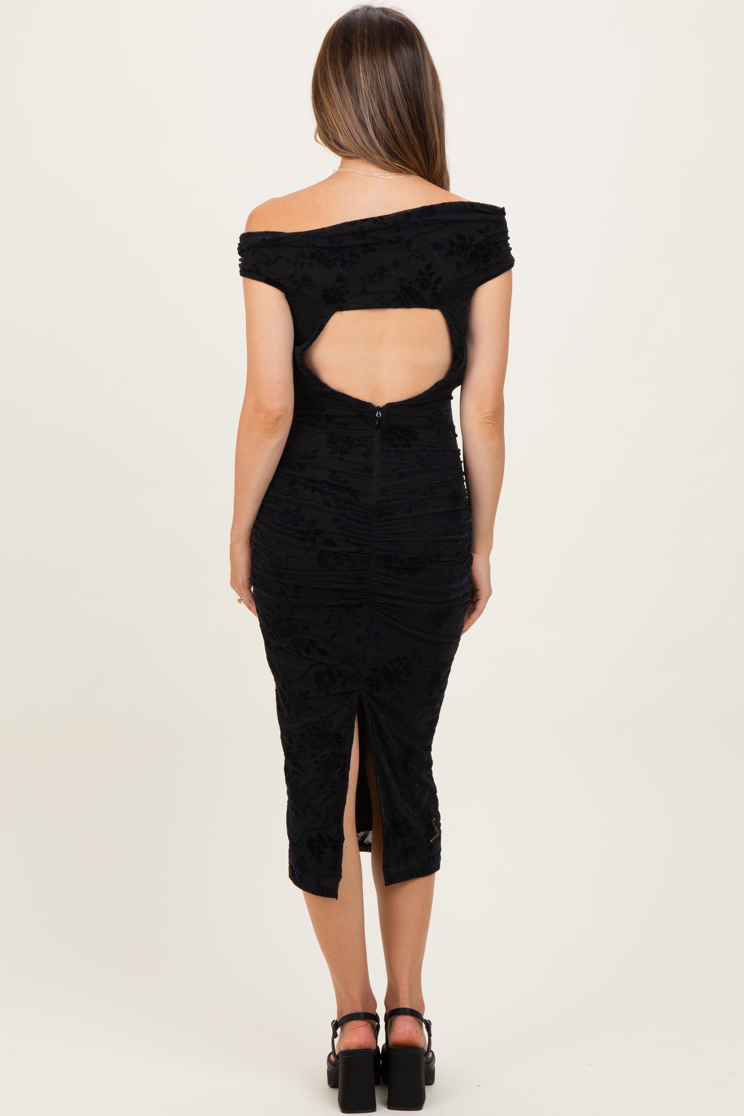 woman wearing a black off-the-shoulder maternity dress with a back cutout and a slit at the hem