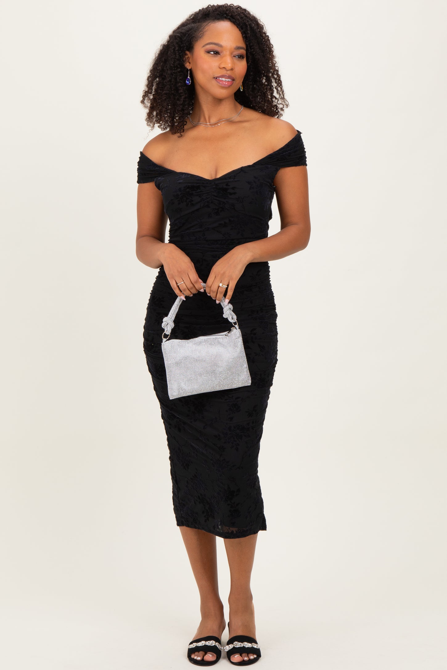 woman wearing a black off-the-shoulder fitted dress with textured details, holding a silver striped handbag