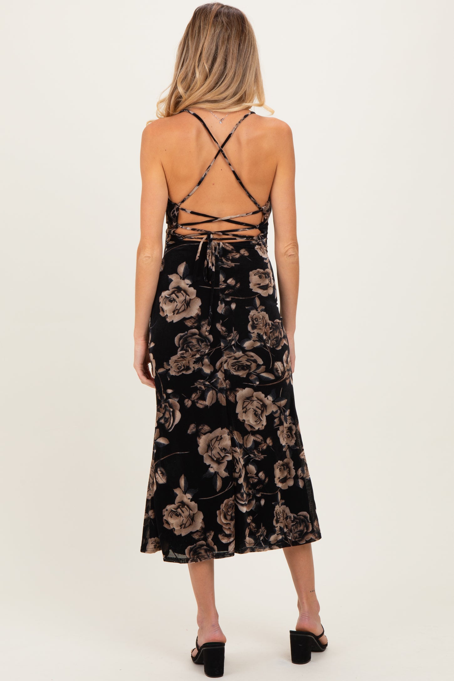 woman wearing a black floral print velvet maternity dress with a crisscross back detail and a mid-length flowy skirt
