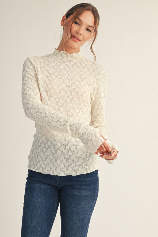 woman wearing a cream long sleeve textured top with a high neckline and fitted sleeves paired with blue jeans