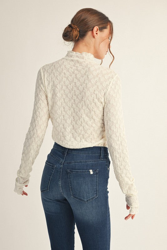woman wearing a cream textured long sleeve top with a high neck and back view, paired with dark blue skinny jeans