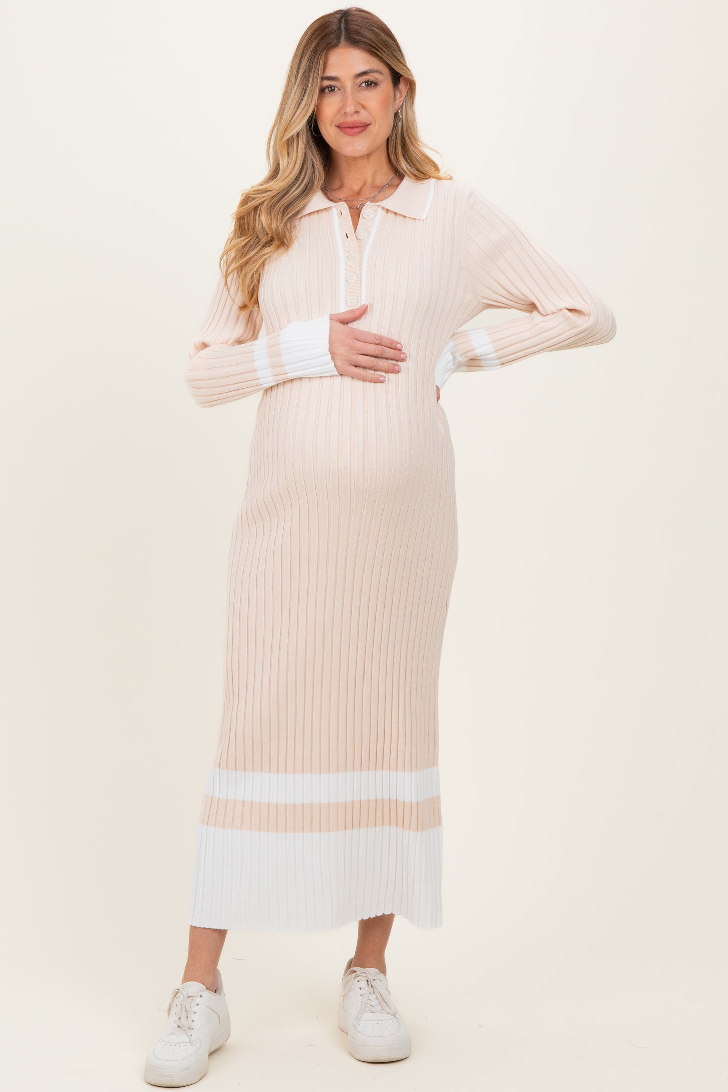 woman wearing a striped pastel pink and white long sleeve maternity dress, holding her baby bump