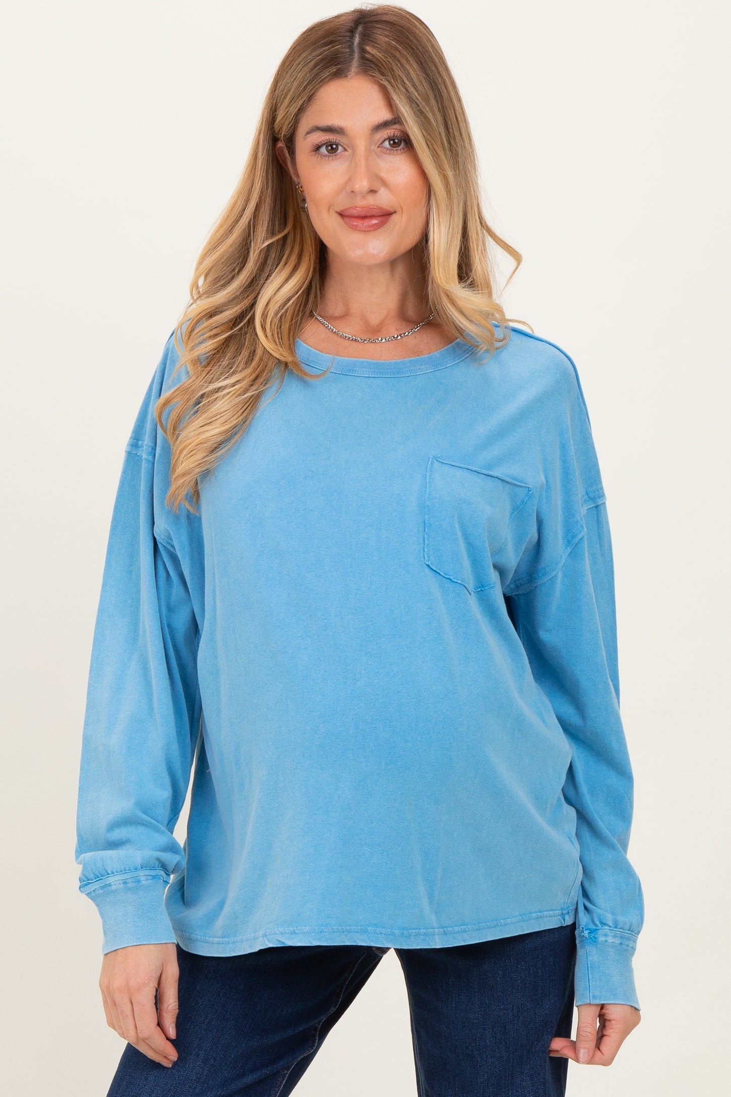 woman wearing a light blue maternity long sleeve top with a front pocket and a subtle relaxed fit