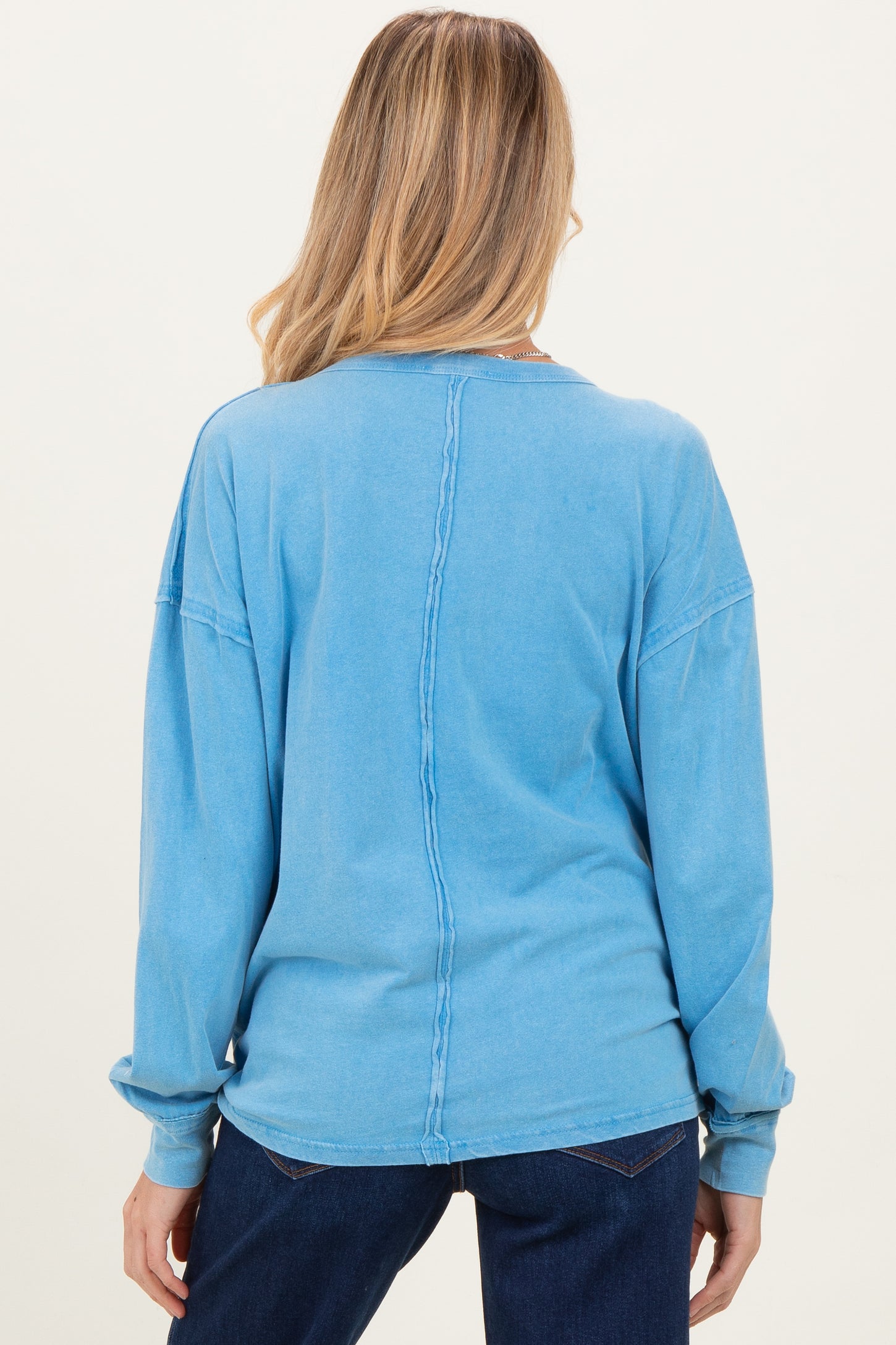 woman wearing a back view of a light blue oversized maternity top with long sleeves and a relaxed fit
