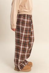 woman wearing brown plaid wide-leg pants, styled casually with a loose beige top and cozy footwear