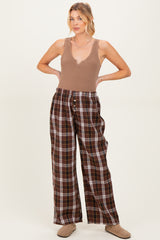 woman wearing a tan ribbed tank top and brown plaid maternity pants with a loose fit and buttons at the waist