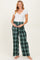 woman wearing a white short sleeve ribbed top and green plaid maternity pants, holding her baby bump